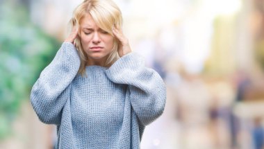 Üzerinde kış kazak giyen genç güzel sarışın kadın izole arka plan baş baş ağrısı için el ile çünkü stres. Migren muzdarip.