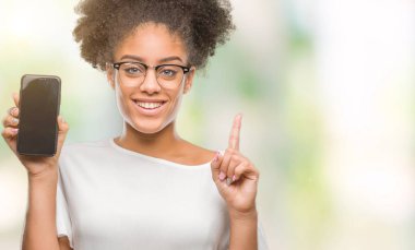 Genç güzel afro Amerikan gösteren smartphone izole arka bir fikirle sürpriz üzerinde ekran ya da gülen yüz, bir numara ile işaret parmağı soru