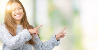 Gülümseyen ve iki elleri ve parmakları ile tarafına işaret kamera bakarak izole arka plan üzerinde kazak giyen genç güzel esmer kadın.