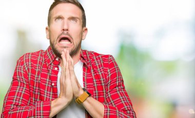 Yakışıklı adam yalvarıyor ve umut ifade yüzünde çok duygusal ve endişe ile birlikte elleriyle dua rahat gömlek giymiş. Bağışlanmak. Din kavramı.