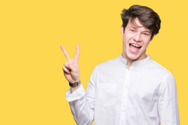 Genç yakışıklı iş adamı mutlu yüz zafer işareti yaparken kameraya göz kırpıyor ile gülümseyen izole arka plan üzerinde. İki numaralı.