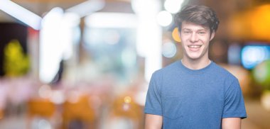 Yüzünde mutlu ve güzel bir gülümseme ile izole arka plan üzerinde mavi t-shirt giyen genç yakışıklı adam. Şanslı kişi.