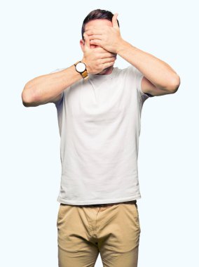 Yakışıklı adam giyiyor rahat beyaz t-shirt kapsayan gözleri ve şaşırttı ve şok ellerle ağız. Duygu gizleme