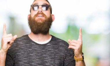 Genç hippi erkek güneş gözlüğü takıyor hayret ve yukarıya bakıp parmakları ile işaret şaşırttı ve silah kaldırdı.