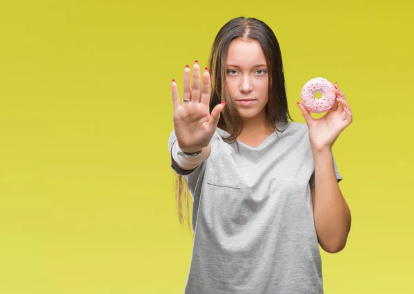 年轻的白种女人吃甜甜甜圈在孤立的背景与开放的手做停止标志与严肃和自信的表达 防御手势 — 图库照片