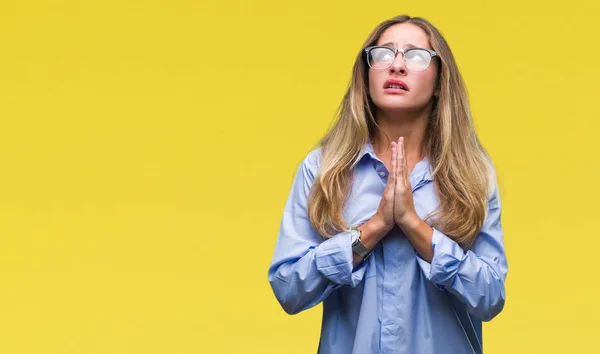 Young beautiful blonde business woman wearing glasses over isolated background begging and praying with hands together with hope expression on face very emotional and worried. Asking for forgiveness. Religion concept.