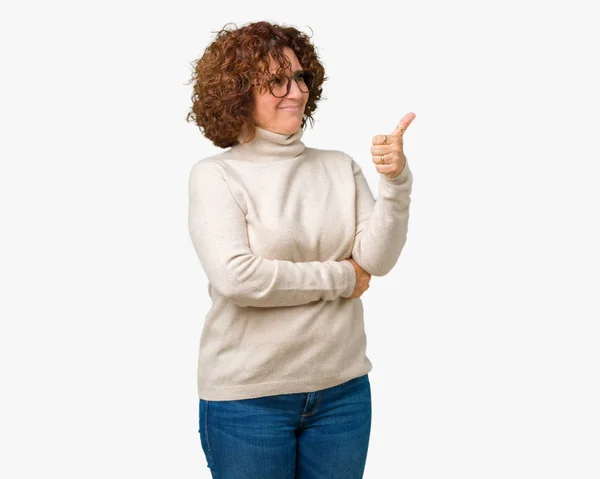 美しい中間エイガー年配の女性見て誇りに思って 孤立した背景にタートルネックのセーターとメガネを着用して笑みを浮かべて親指側にジェスチャーを — ストック写真