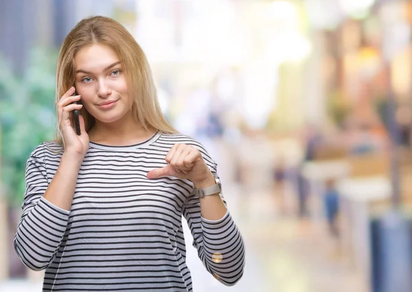 Young caucasian woman showing smartphone screen over isolated background with surprise face pointing finger to himself