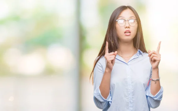 年轻的亚洲商业妇女戴着眼镜在孤立的背景下惊讶和惊讶地看着手指和举起手臂 — 图库照片