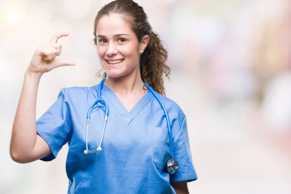 年轻的黑发医生女孩穿着护士或外科医生制服在孤立的背景微笑和自信的手势与手做大小标志用手指 而看和相机 测量概念 — 图库照片