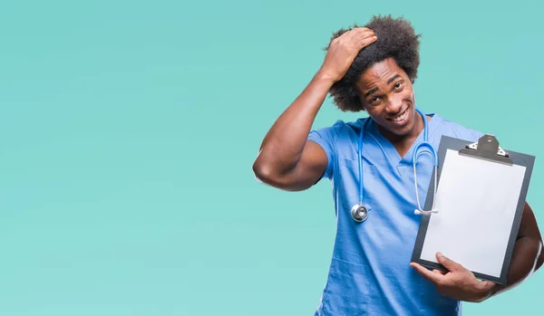 Afro american surgeon doctor holding clipboard man over isolated background stressed with hand on head, shocked with shame and surprise face, angry and frustrated. Fear and upset for mistake.
