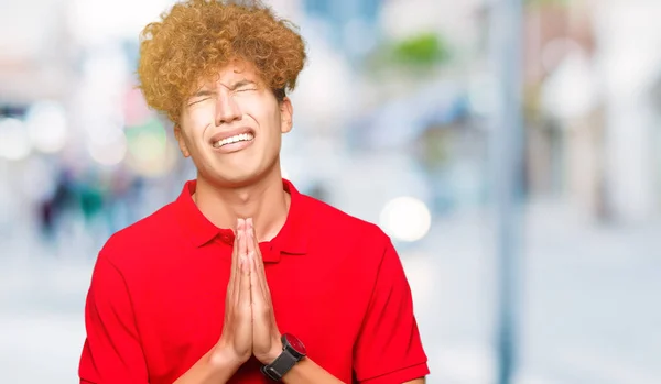 Όμορφος Νεαρός Άφρο Μαλλιά Φορώντας Κόκκινο Shirt Επαιτεία Και Προσεύχεται — Φωτογραφία Αρχείου