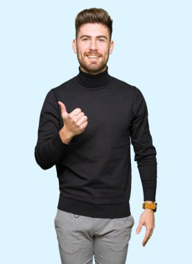 Hareketi el ile mutlu yaşasın yapıyor kış kazak giyen genç yakışıklı sarışın adam. Kameraya bakarak başarı gösteren ile ifade onaylama.