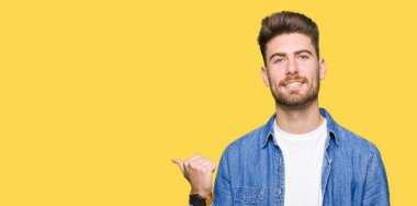 Seyir ve başparmak yanında yukarıyı mutlu yüz ile gülümseyen rahat denim ceket giyen genç yakışıklı sarışın adam.