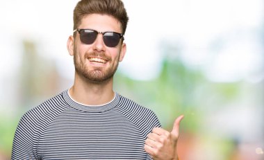 Genç yakışıklı adam hareketi el ile mutlu yaşasın yaparken güneş gözlüğü takıyor. Kameraya bakarak başarı gösteren ile ifade onaylama.