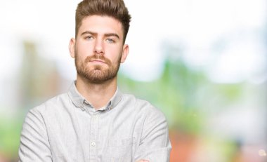 Gündelik gömlek giyen, kuşkucu ve gergin genç yakışıklı bir adam. Yüzünde çapraz kollu tasvip etmeyen bir ifade var. negatif kişi.