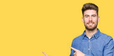 Genç yakışıklı sarışın adam giyiyor rahat kot gömlek gülümseyen ve iki elleri ve parmakları ile tarafına işaret kamera bakıyor.