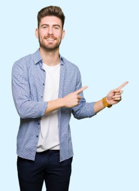 Genç yakışıklı sarışın adam rahat forması giyen gülümseyen ve iki elleri ve parmakları ile tarafına işaret kamera bakıyor.