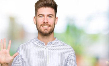 Genç ve yakışıklı bir adam kendini beğenmiş ve mutlu bir şekilde gülümserken beş numarayı işaret ediyor..