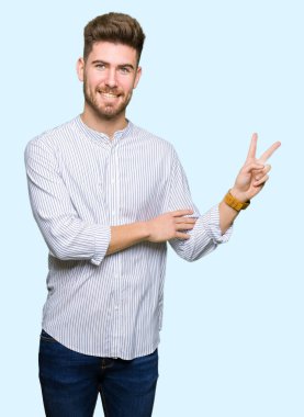 Genç, yakışıklı, gülümseyen ve kameraya göz kırpan bir adam zafer işareti yapıyor. İki numara..