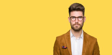 Gevşek ciddi ifade ile yüzünde gözlüklü genç yakışıklı iş adamı. Basit ve doğal kameraya bakıyor.