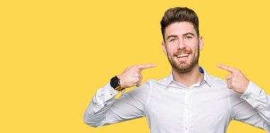 Kendinden emin gösterilen ve işaret parmakları diş ve ağız ile gülümseyen genç yakışıklı iş adamı. Sağlık kavramı.