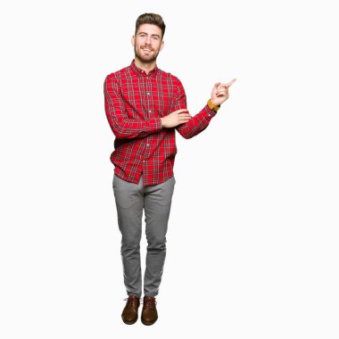 Kameraya bakarak yan el ve parmak ile işaret eden genç yakışıklı adam yüzünde kocaman bir gülümseme ile.