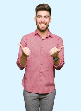 El ile olumlu hareketi yaparken genç yakışıklı iş casual adam başarı işareti başparmak gülümseyen ve mutlu. Neşeli bir ifadeyle, kazanan jest kameraya bakıyor.