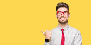 Seyir ve başparmak yanında yukarıyı mutlu yüz ile gülümseyen gözlüklü genç yakışıklı iş adamı.