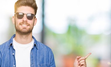 Kameraya bakarak yan el ve parmak ile işaret yüzünde, kocaman bir gülümseme ile kot ceket giyen genç yakışıklı zarif adam.