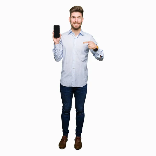 Young handsome man business showing smartphone screen with surprise face pointing finger to himself