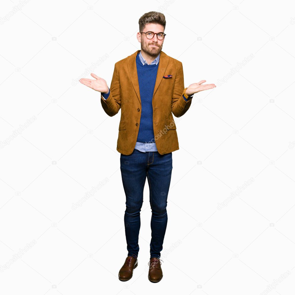 Young handsome business man wearing glasses clueless and confused expression with arms and hands raised. Doubt concept.