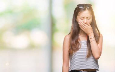 Genç Asyalı kadın güneş gözlüğü takıyor izole arka plan üzerinde el ile ağız kapsayan yorgun esneme sıkılmış. Restless ve uyku hali.