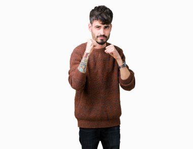 Genç yakışıklı adam giyen kış kazak izole arka plan üzerinde hazır yumruk savunma hareketi, kızgın ve üzgün yüz, sorunu korkuyor ile mücadele