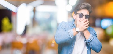 Yakışıklı delikanlı üzerinde güneş gözlüğü takıyor arka plan ağız hata için elleriyle kapsayan şok izole. Gizli kavramı.