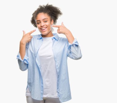 Kendinden emin gösterilen ve işaret parmakları diş ve ağız ile gülümseyen izole arka plan üzerinde genç afro Amerikalı kadın. Sağlık kavramı.