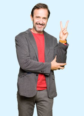 Orta yaş yakışıklı iş adamı mutlu yüz zafer işareti yaparken kameraya göz kırpıyor ile gülümseyen. İki numaralı.