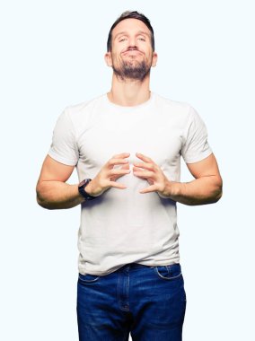 Yakışıklı adamın Casual beyaz t-shirt eller birlikte giydiğini ve parmakları rahat ve neşeli gülümseyen geçti. Başarı ve iyimser