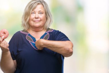 Kıdemli artı boyutu ile arka plan beyaz kadın üzerinde şeker donut yemek izole için kendini parmakla yüz sürpriz