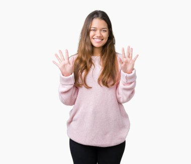 Gösterilen ve parmakları ile işaret izole arka plan üzerinde pembe kış kazak giyen genç güzel esmer kadın kendinden emin ve mutlu gülümseyerek süre on numara.