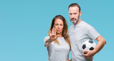 Orta yaş İspanyol çift ile izole arka plan üzerinde futbol futbol topu tutan el dur işareti ile ciddi ve kendine güvenen ifade, savunma jest yapıyor açın