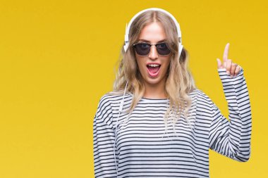 Başarılı fikirle parmağı yukarıyı izole arka plan üzerinde kulaklık ve güneş gözlüğü giyen güzel genç sarışın kadın. Çıktıktan ve mutlu. Bir numara.