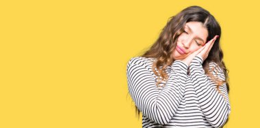 Rüya ve elleri ile kapalı gözler gülümseyen birlikte poz çizgili süveter uyku giyen genç güzel kadın yorgun.