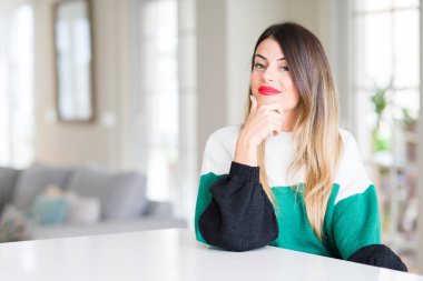 Evde kış kazak giyen genç güzel kadın emin çapraz kollar ve çeneme kaldırdı el ile gülümseme ile kameraya bakıyor. Pozitif düşünce.