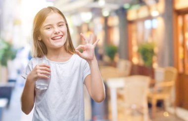 Genç güzel kız parmak, mükemmel sembolü ile ok işareti yapıyor izole arka plan üzerinde bardak su içme