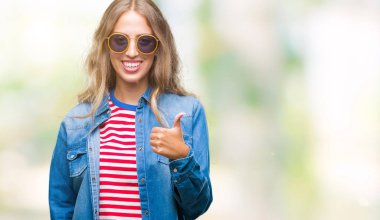 Güzel genç sarışın kadın hareketi el ile mutlu yaşasın yapıyor izole arka plan üzerinde güneş gözlüğü takıyor. Kameraya bakarak başarı gösteren ile ifade onaylama.