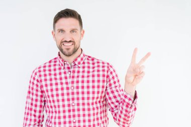Mutlu yüz zafer işareti yaparken kameraya göz kırpıyor ile gülümseyen izole arka plan üzerinde gömlek giymiş yakışıklı delikanlı. İki numaralı.