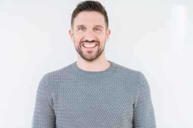 Genç yakışıklı adam yüzünde mutlu ve güzel bir gülümseme ile izole arka plan üzerinde rahat kazak giyiyor. Şanslı kişi.