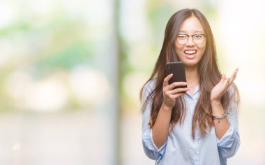 Genç Asyalı kadın manifatura üzerinden Smartphone kullanarak büyük gülümseme ile çığlık zaferini kutluyor arka plan çok mutlu ve heyecanlı, kazanan ifade izole ve ellerini kaldırdı