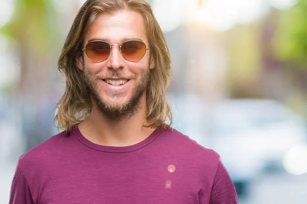 Young handsome man with long hair wearing sunglasses over isolated background with a happy and cool smile on face. Lucky person.